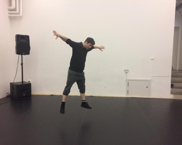 Mikko Hyvönen in a white dance studio, jumping hands wide apart, looking at the ground