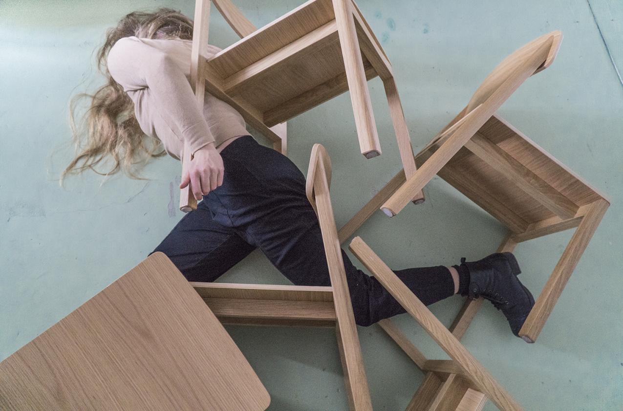A person is partly laying under fallen chairs, holding on to them