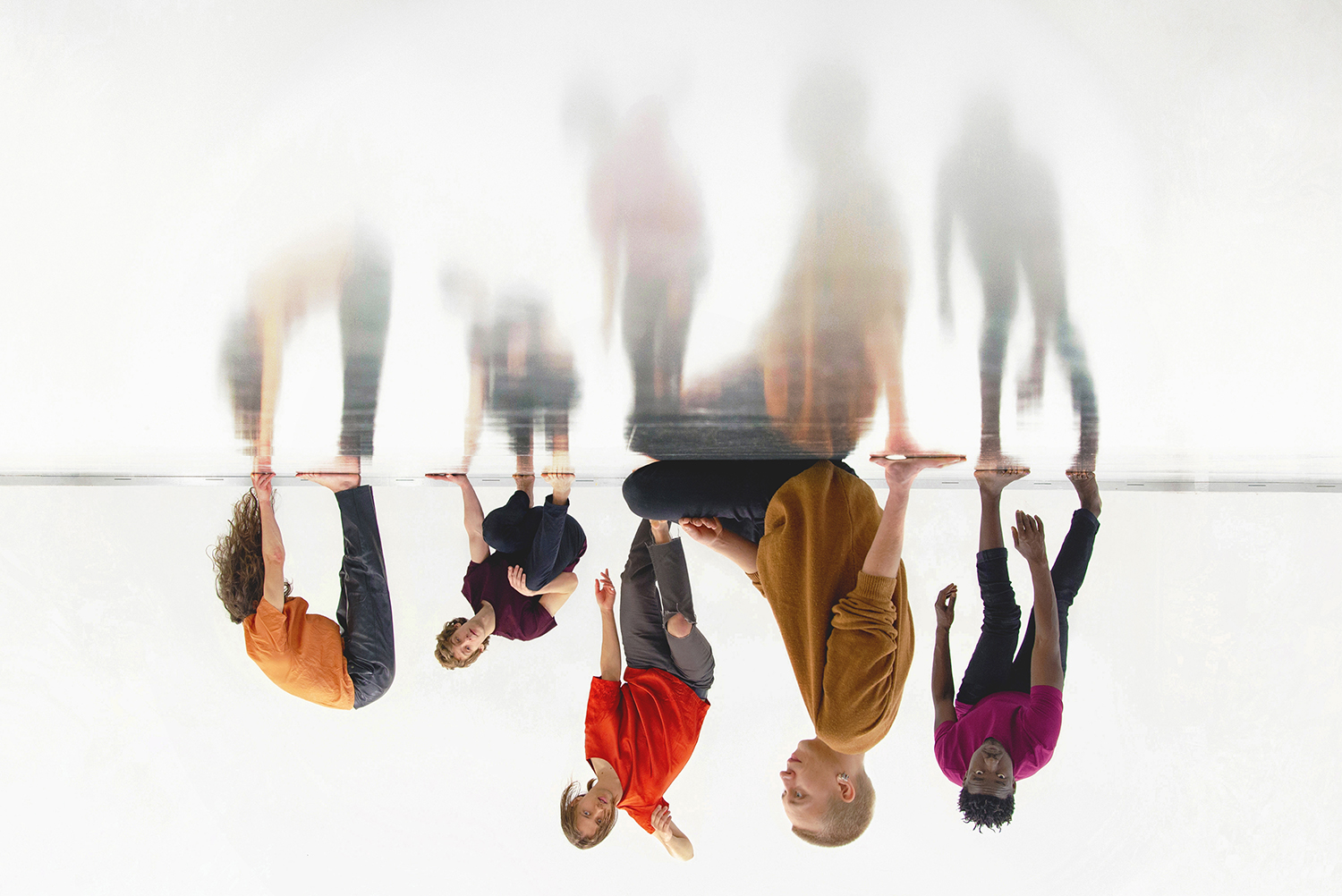 Viisi henkilö istuu ja seisoo eri asennoissa heijastavalla pinnalla ylösalaisin olevassa kuvassa. oel