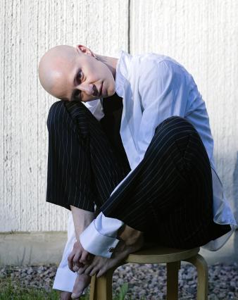 Artist Teo Ala-Ruona sitting on a chair with his legs up, leaning his head on his knees.