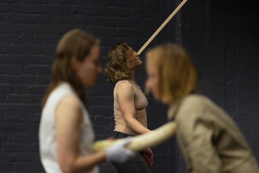 Photo: Katri Naukkarinen Three performers. The photo focus is on the performer at the back. They are holding a long stick on their nose.