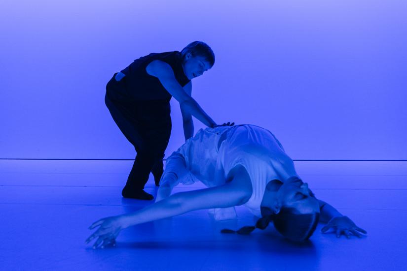 Two dancers. One of the is bent backwards on the floor. The photo is very blue.