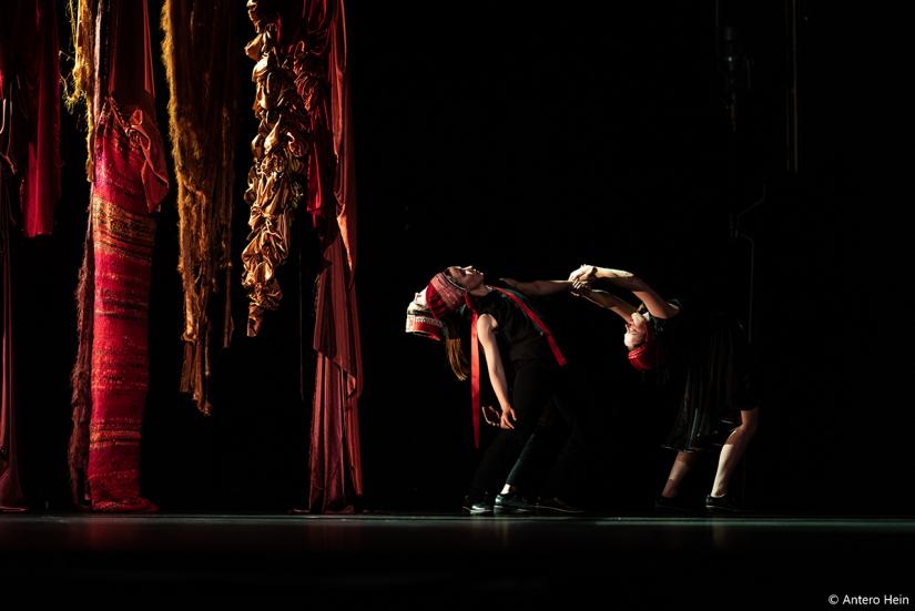 A stage with big, colourful hanging cloths. There are also two performers in the photo.