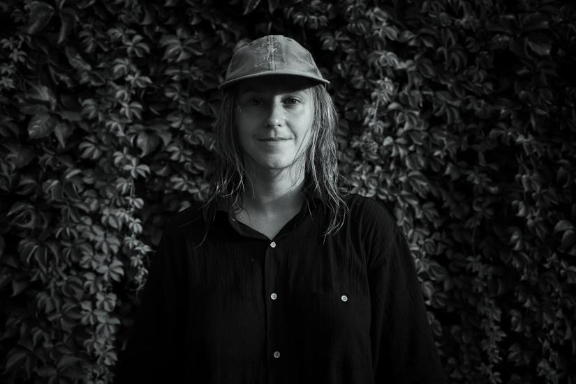 Linda Blomqvist mustavalkoisessa kuvassa keskellä, lippalakki päässä, tumma kauluspaita päällä. Hän hymyilee.