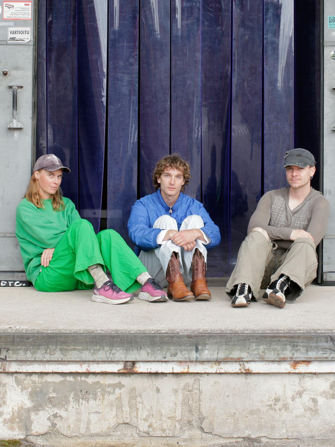  The three artists sitting together in front of a dark blue plastic stip curtains.