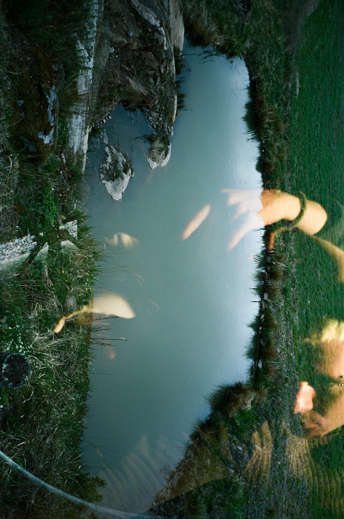 A picture from a pond's reflective surface, with a person reflecting from it.