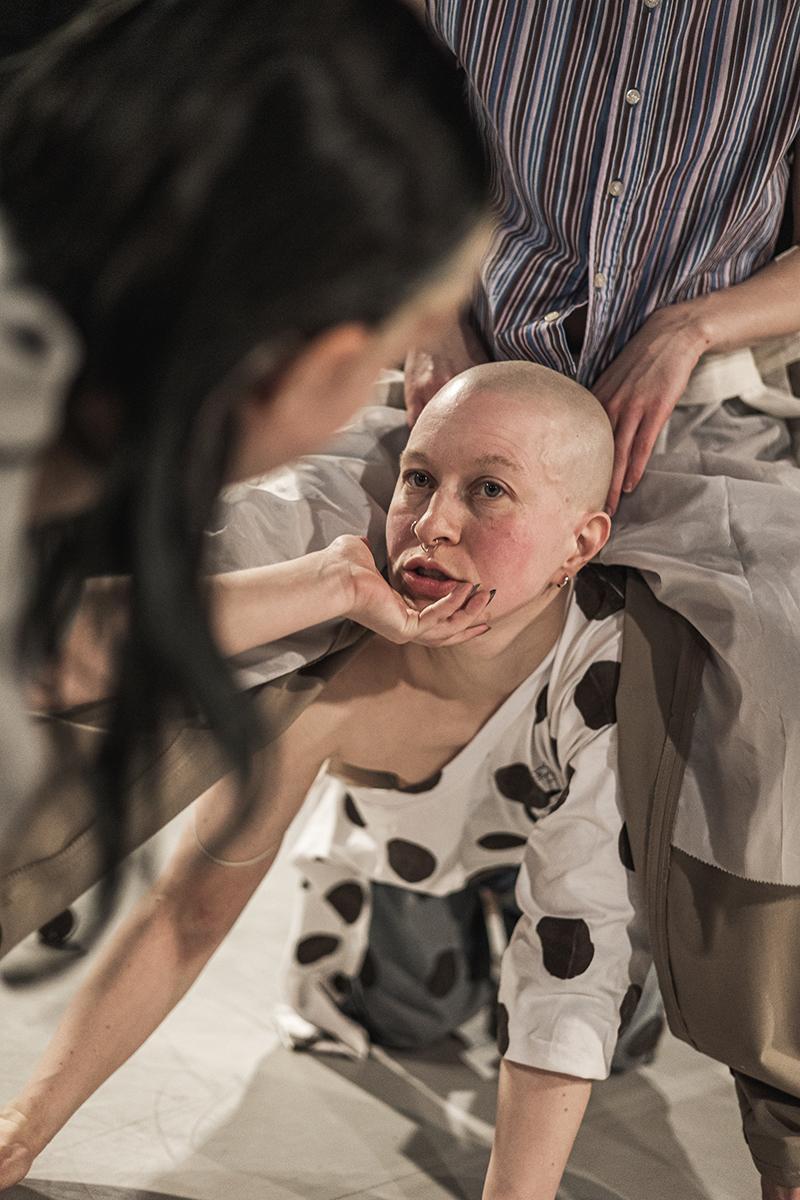 Dancers face in the middle, with someone on their back and another person holding their face with one hand.