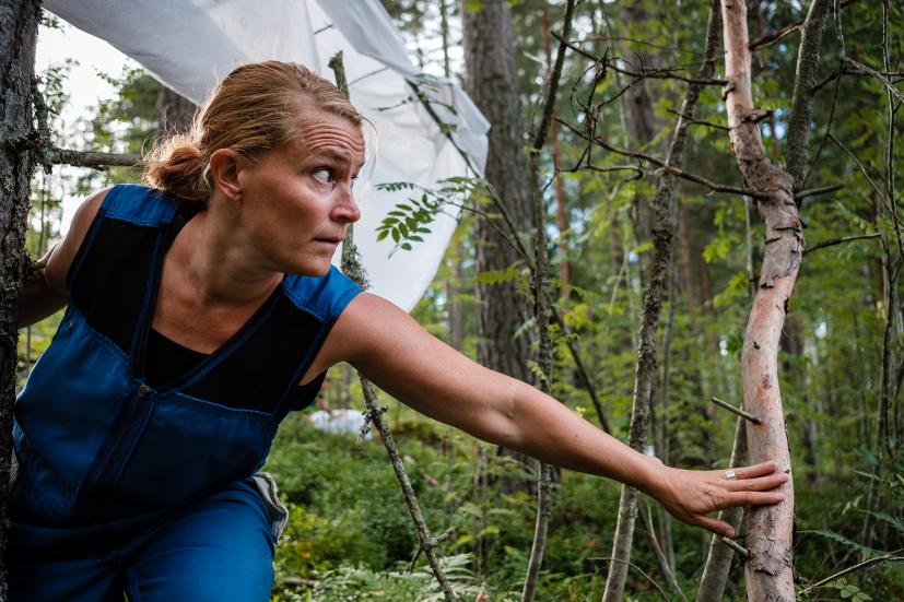 Performer in the forrest, wearing blue overalls.