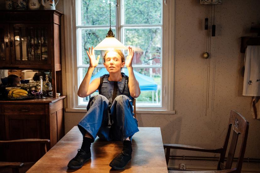 Performes is sitting on a table in a kitchen, wearing blue overalls.