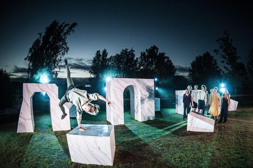 Yksi henkilö tekee parkour-liikettä yhden käden varassa. Muut esiintyjät katsovat.