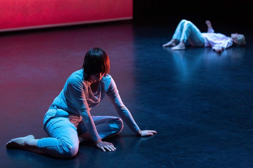 Two dancers. One is sitting on the floor. The other is lying on their back.