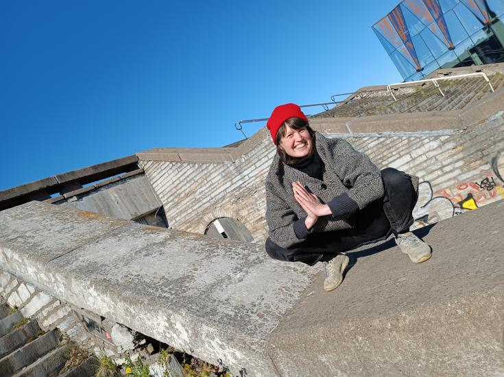 Kati Raatikainen hymyilee kyykyssä betonimaiseman ympäröimänä