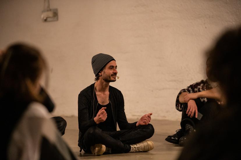 Raphaël Beau istumassa risti-istunnassa lattialla puhumassa ympärillä oleville ihmisille