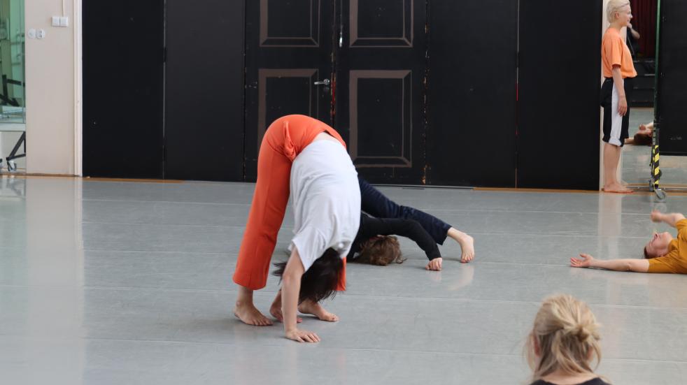 In an white studio a person is bending their head toward the knees.