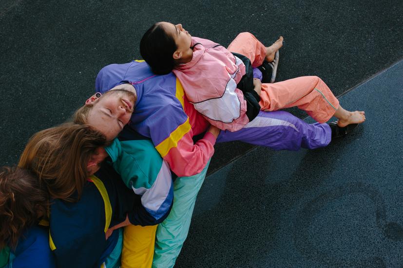 People wearing colourful clothes are leaning on each other, all in a heap.