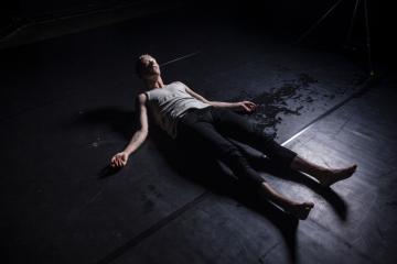 Artist Teo Ala-Ruona lying down on a black floor, with a see-through jelly mask on.