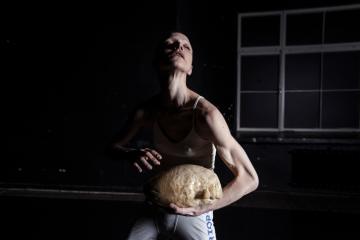 Performer Mina Tomic standing in a shadow holding a head made of jelly.