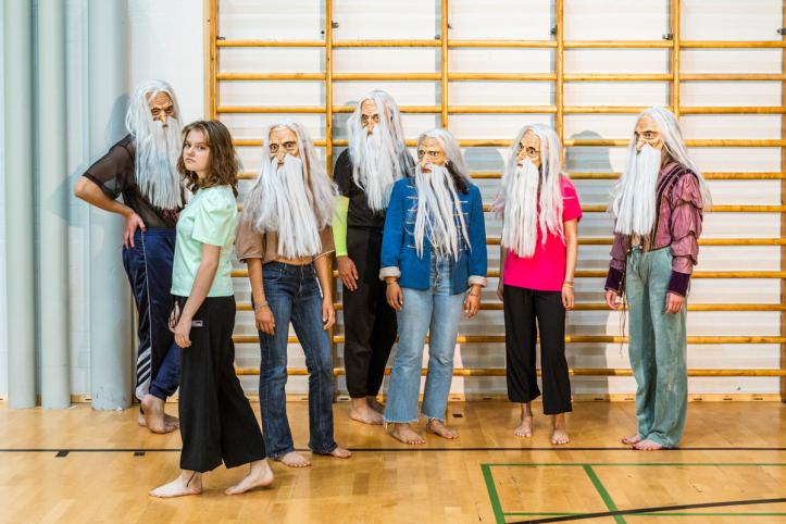 Ryhmä nuoria seisoo koulun liikuntasalissa. Yhtä lukuunottamatta eillä on päässään naamiot. Naamiot esittävät vanhaa miestä, jolla on pitkä valkoinen parta ja tukka.