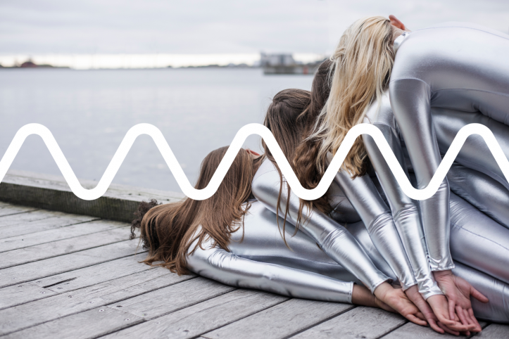 Five people, dresses in shiny silve outfits, are lying on top of each other on a pier.