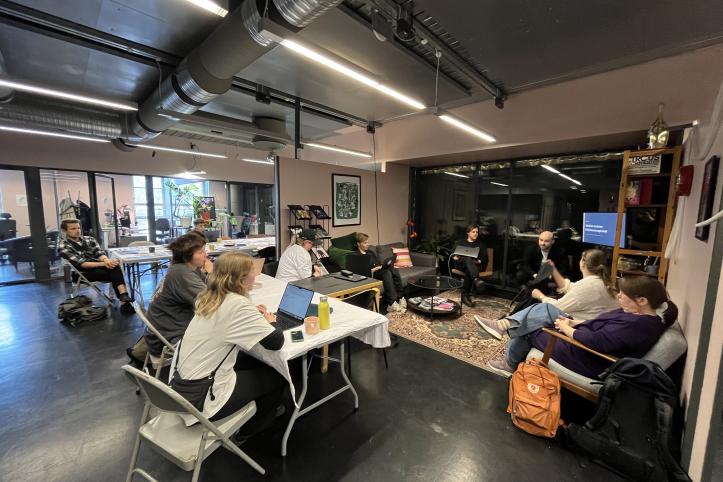 A gropu of people are sitting in a loose cirle. The space is an ofice.