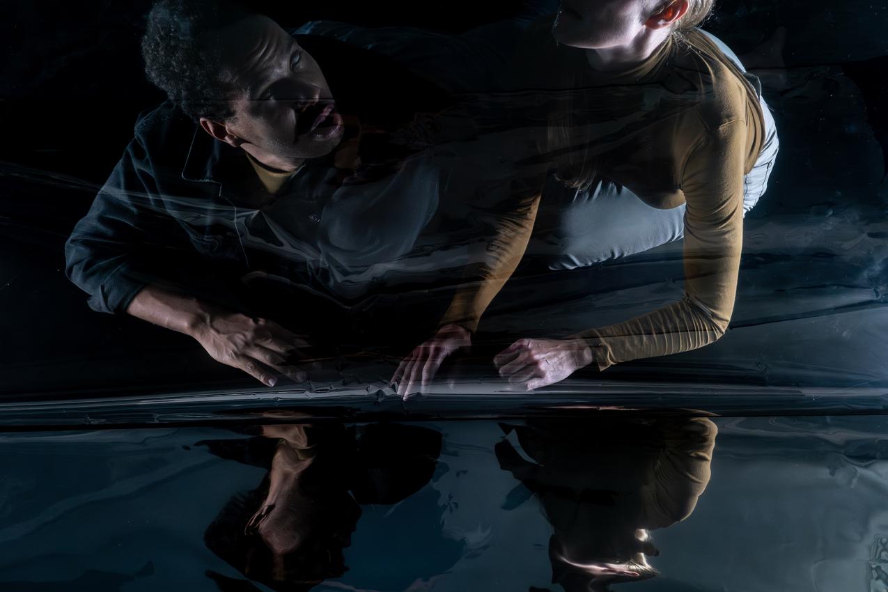 Two people are sitting next to a reflecting surface.