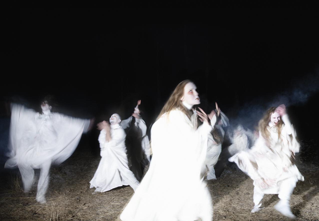 People dressed in white, dancing on a dark field.