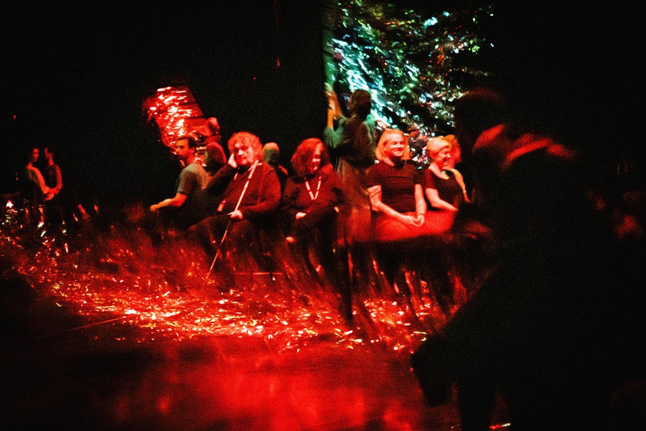 Audience in a circle, in a red lighted space