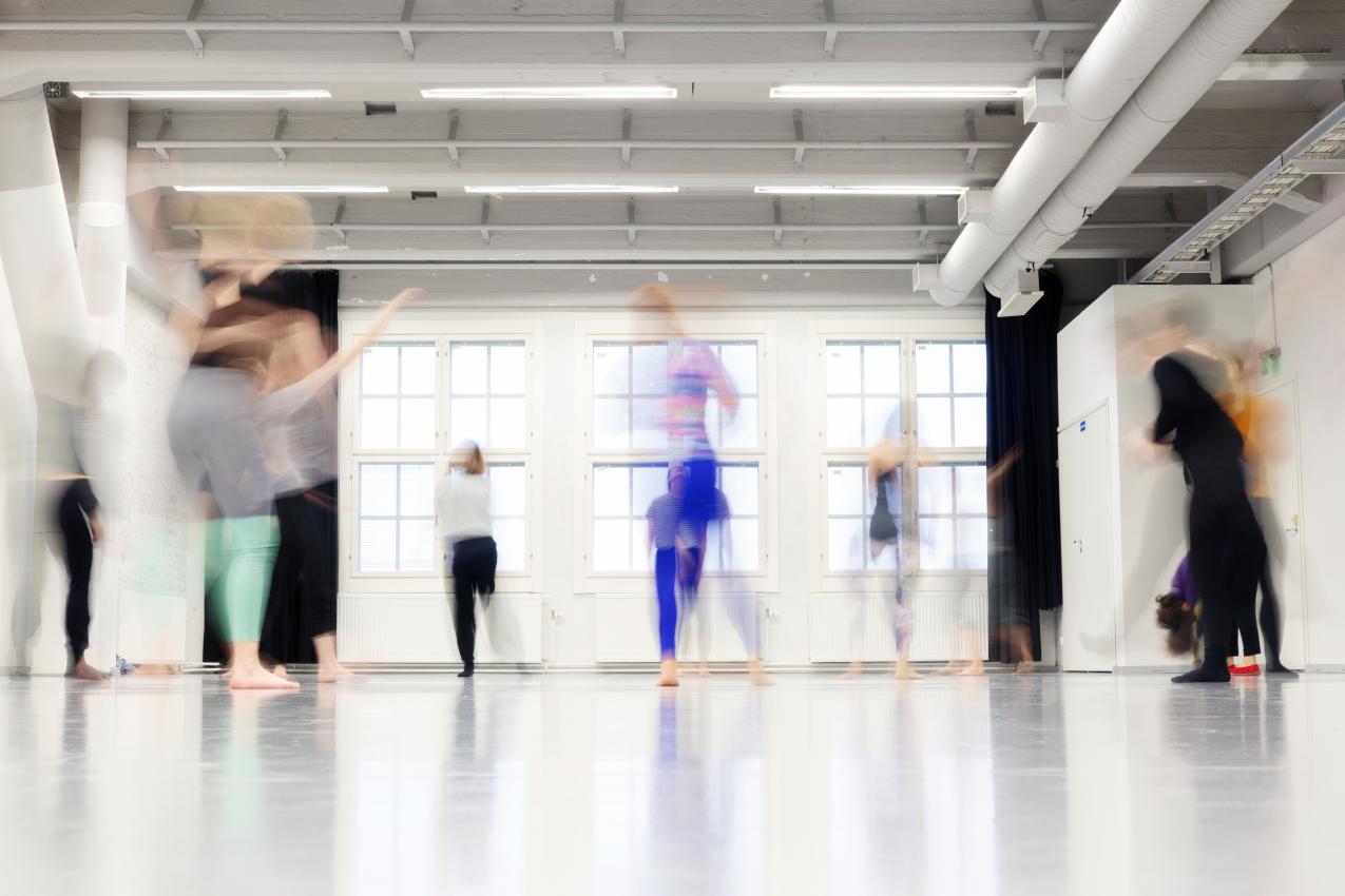 Blurry figures dancing in a large, light dance studio.