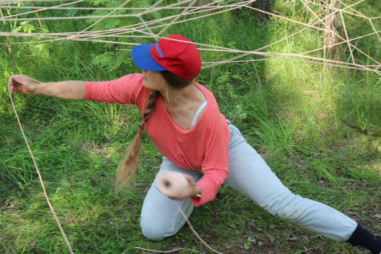 A person on their knees making a web from yarn.