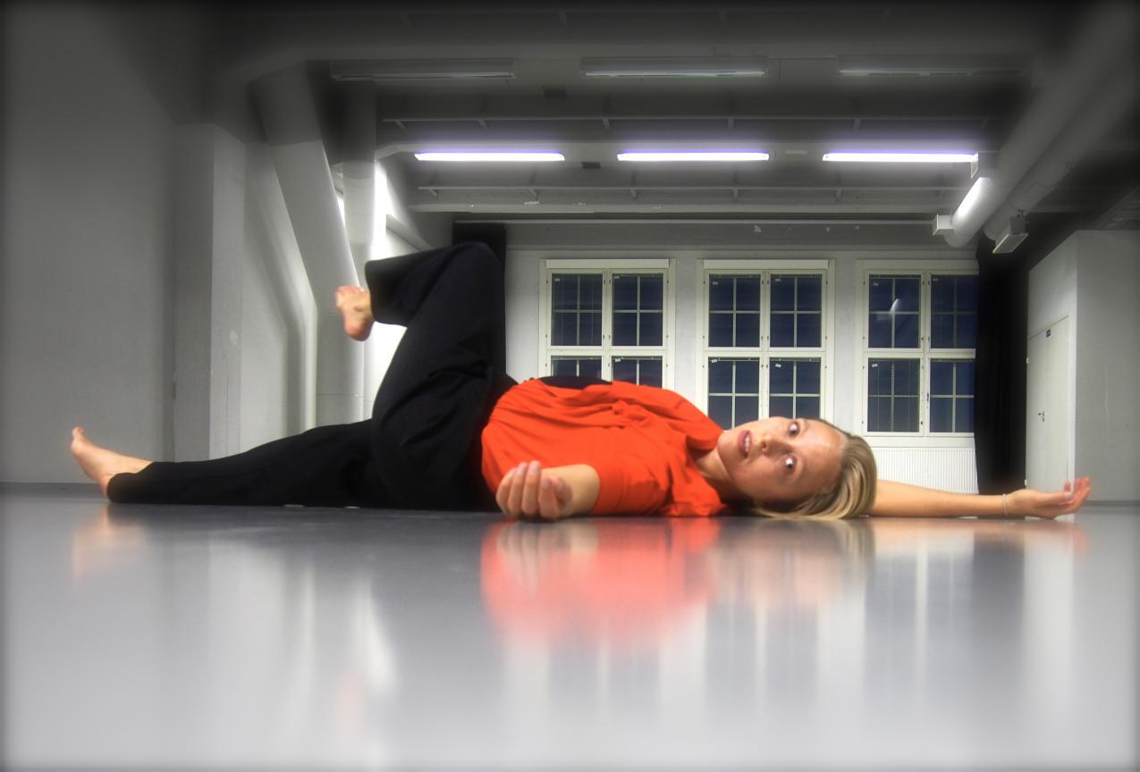 Tanssija makaa selällään lattialla punaisessa paidassa