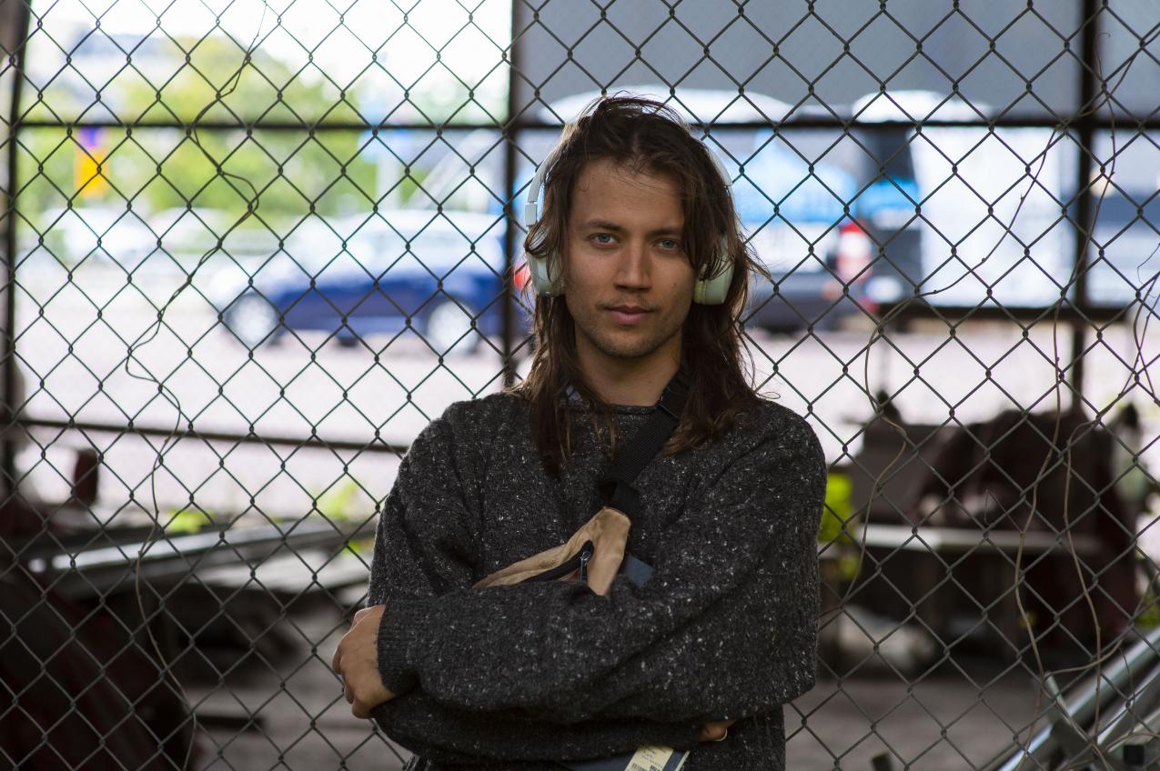 Person leaning on mesh fence, with earphones over their ears, looking at the camera