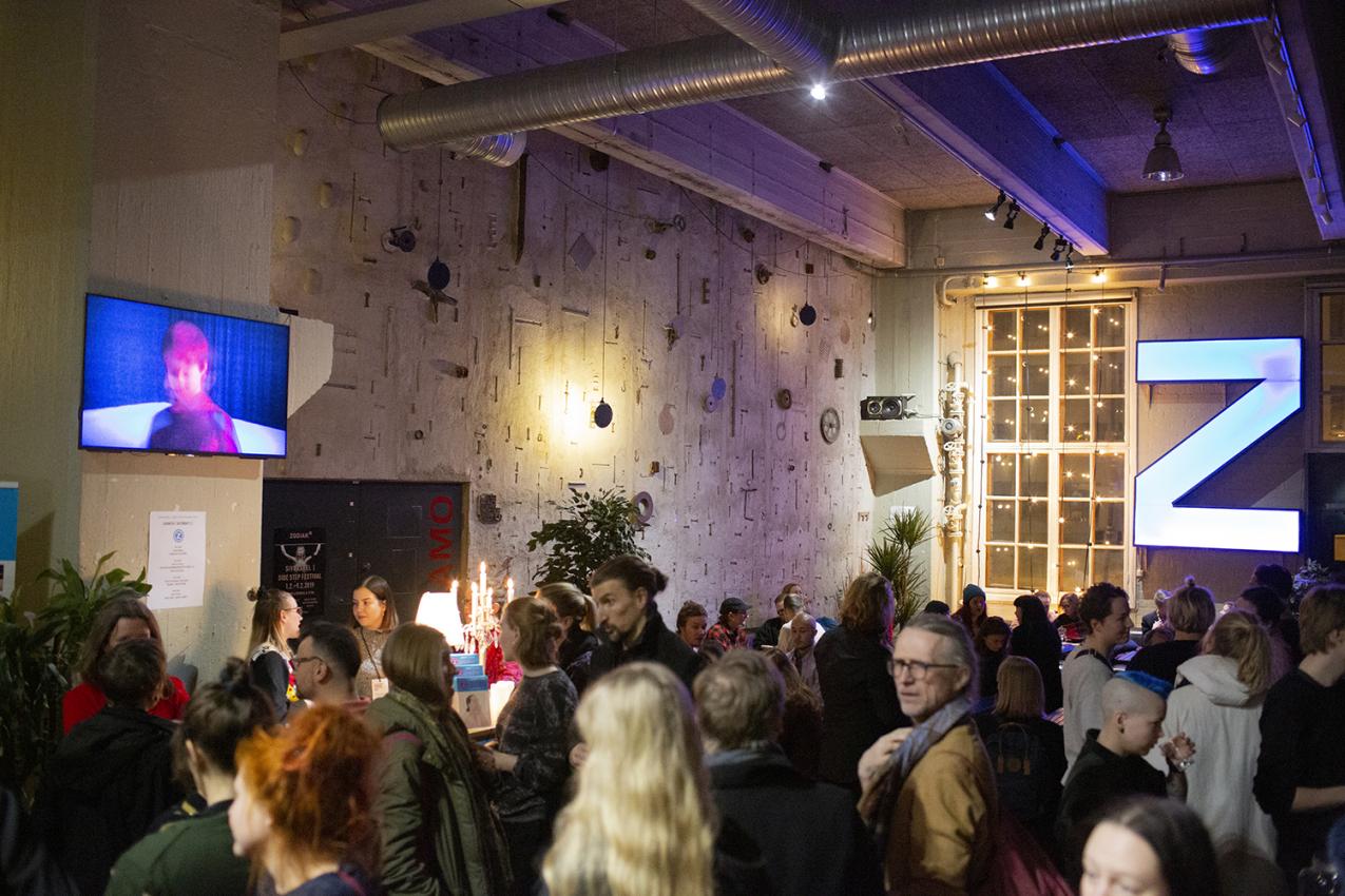 Audience in a foyer. At the background a large light-Z on a wall.