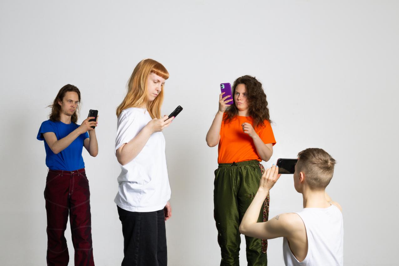 The performers in a marketing photo. They are all looking at their phones