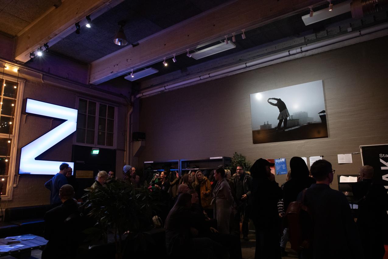 Audience in a foyer. At the background a large light-Z on a wall.