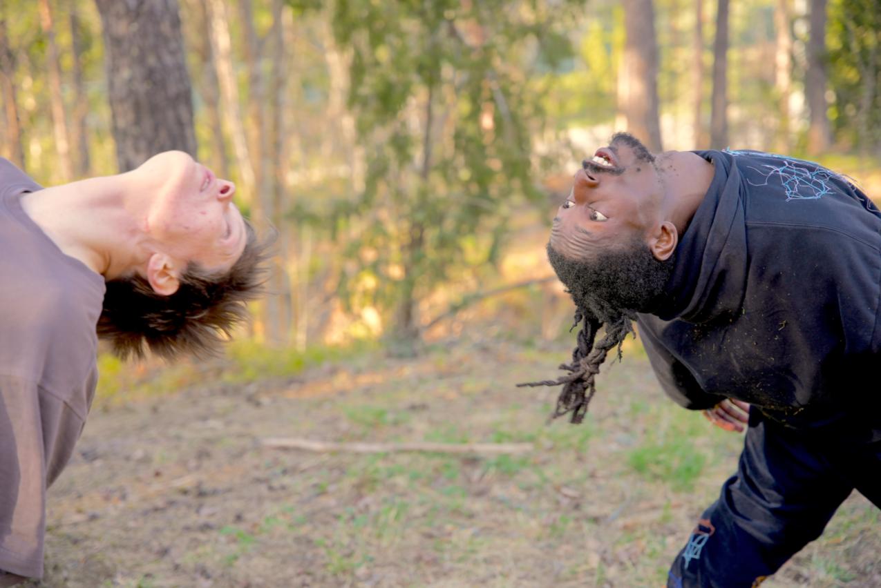 People are standing their back to each other. They are looking at each other by bending their heads backwards.
