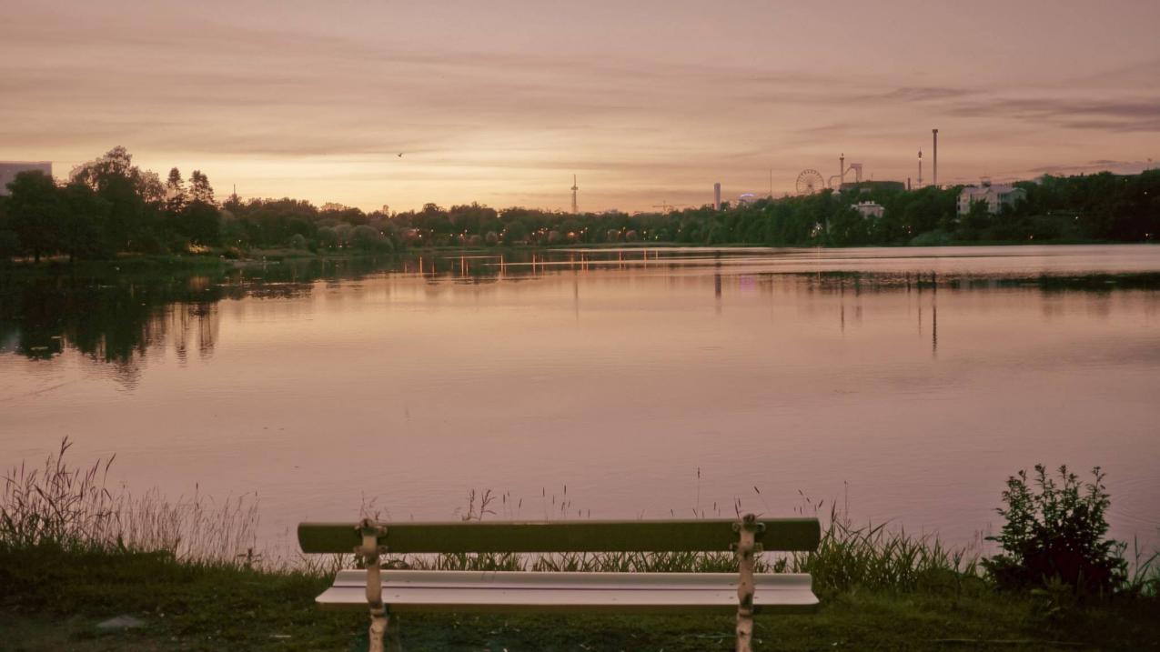 Töölönlahti iltahämärässä. Rannalla on tyhjä puiston penkki.