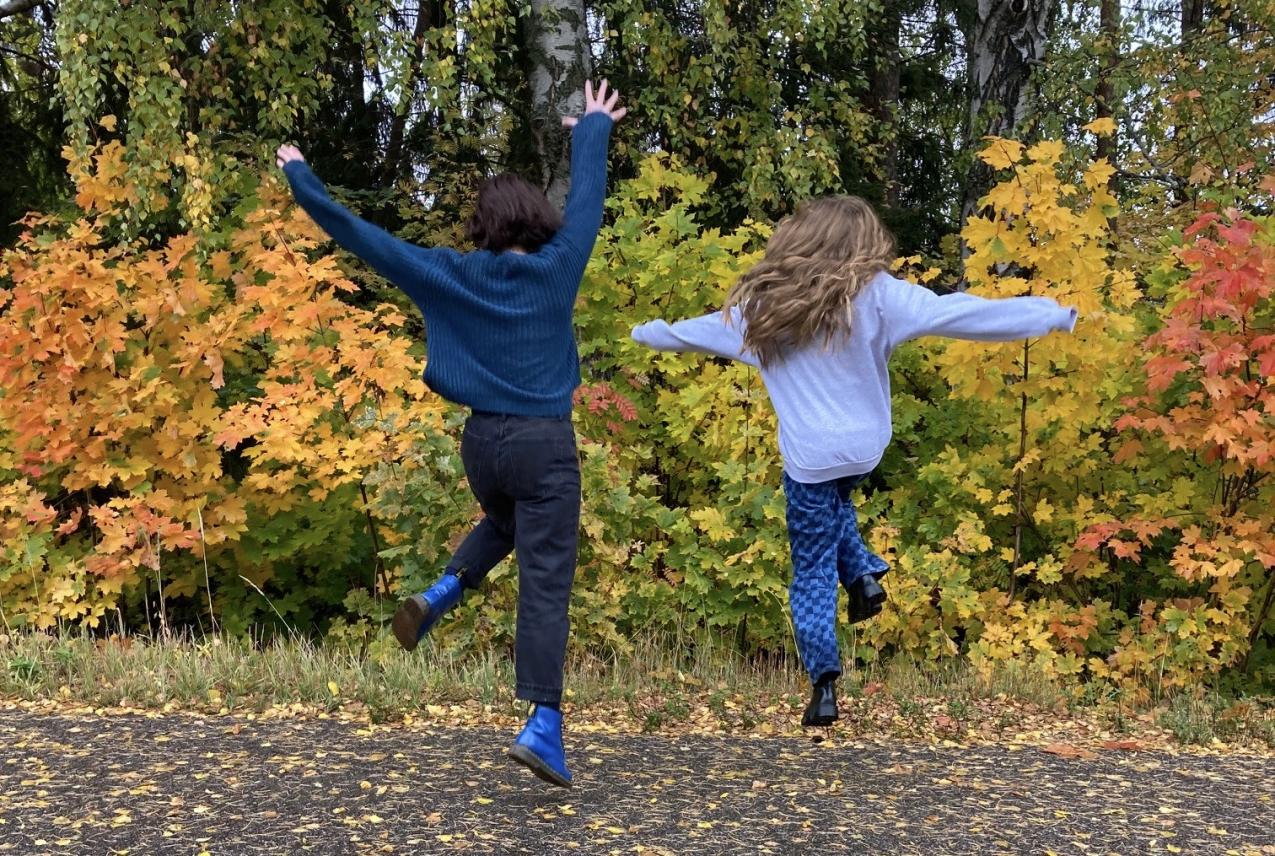 Aikuinen ja lapsi hyppäävät ilmaan syksyisessä maisemassa