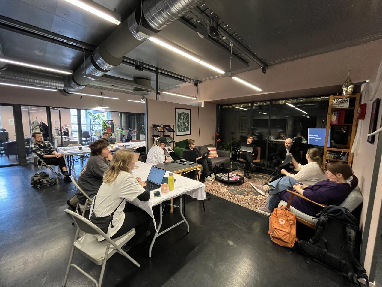 A gropu of people are sitting in a loose cirle. The space is an ofice.