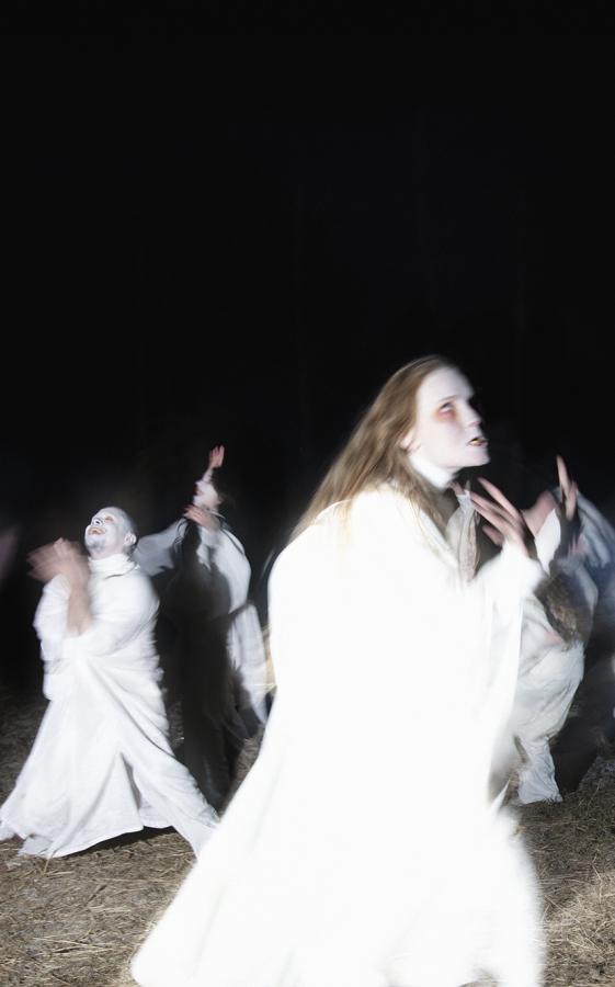 Figures dressed in all white. They are dancing on a field in the dark.