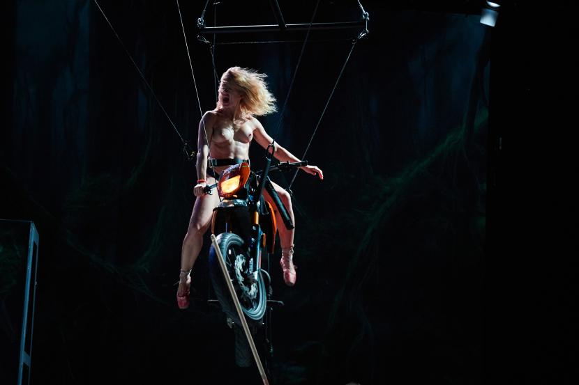 A naked woman is sitting on a motorcycle. The motorcycle is hanging in the air.