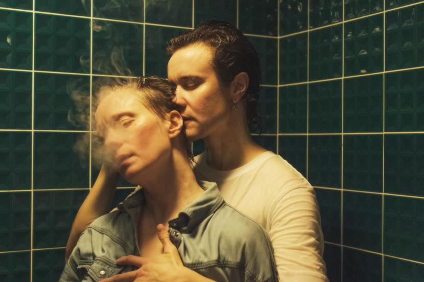 PR photo of two people standing in a shower. The walls are covered with green tiles.