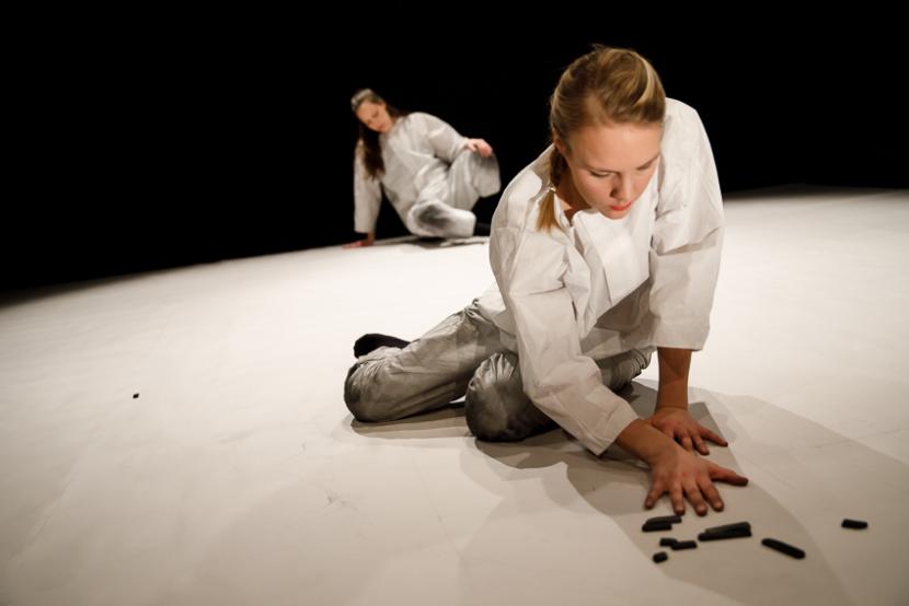 Two people sitting on the floor wearing white jumpsuits, exploring something on the floor