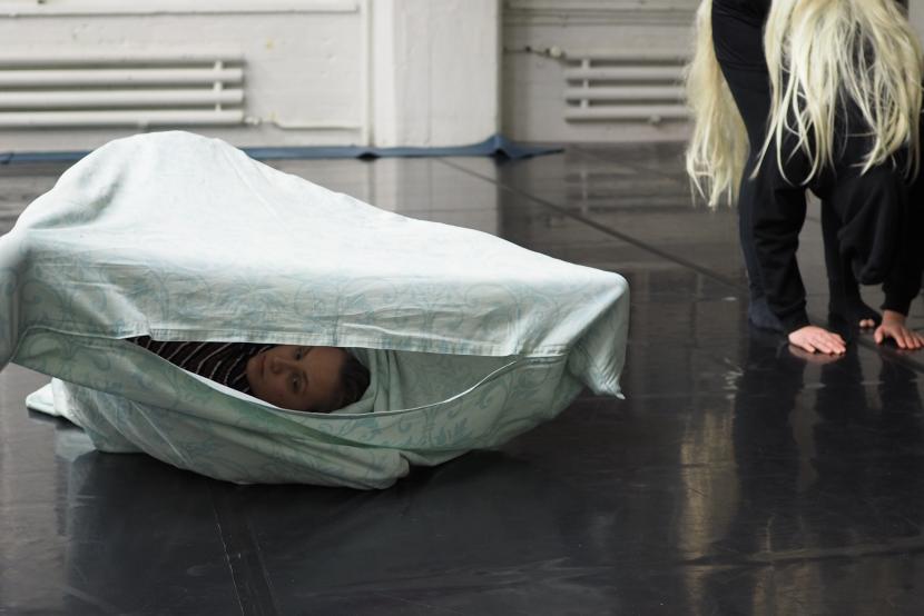 Tuuli Vahtola hiding inside a white cloth, just a bit of her head is visible. There is also another person in the space. 