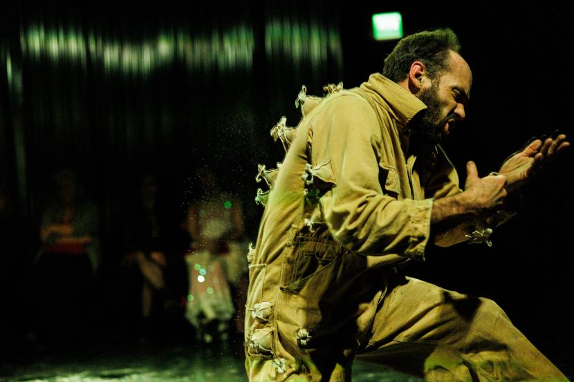 Ryan Mason dancing on darkish space. He is twisted to the side with hand and head turned to the side. 