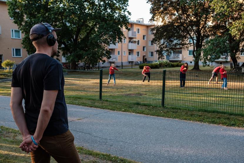 A person wearing headphones, is watching some people, who are wearing red.