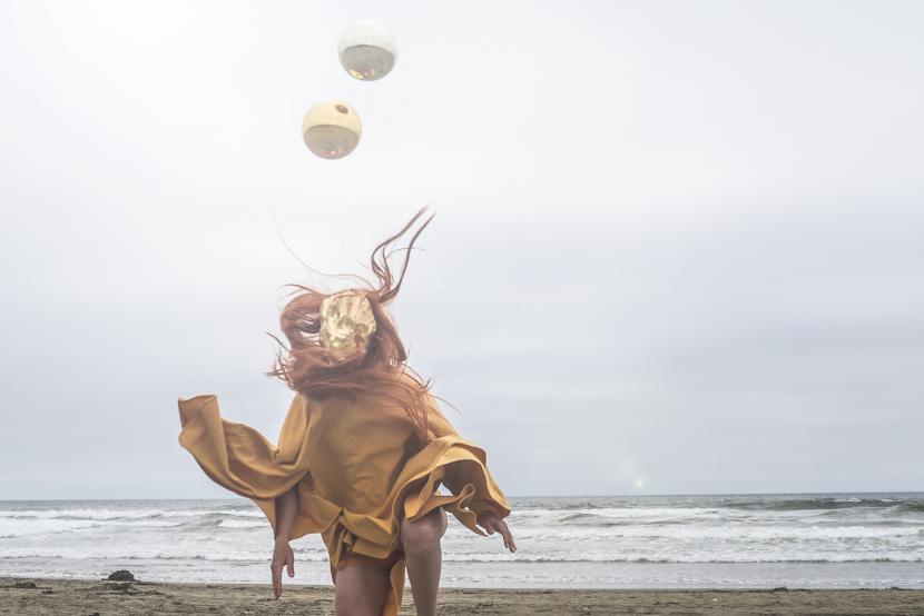 A figure, wearing floaty clothes, on a beach