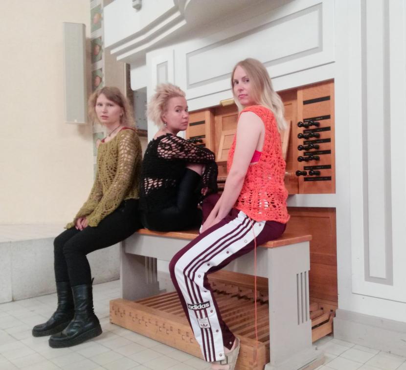Kolme naisoletettua istuu penkillä. He katsovat kameraan.