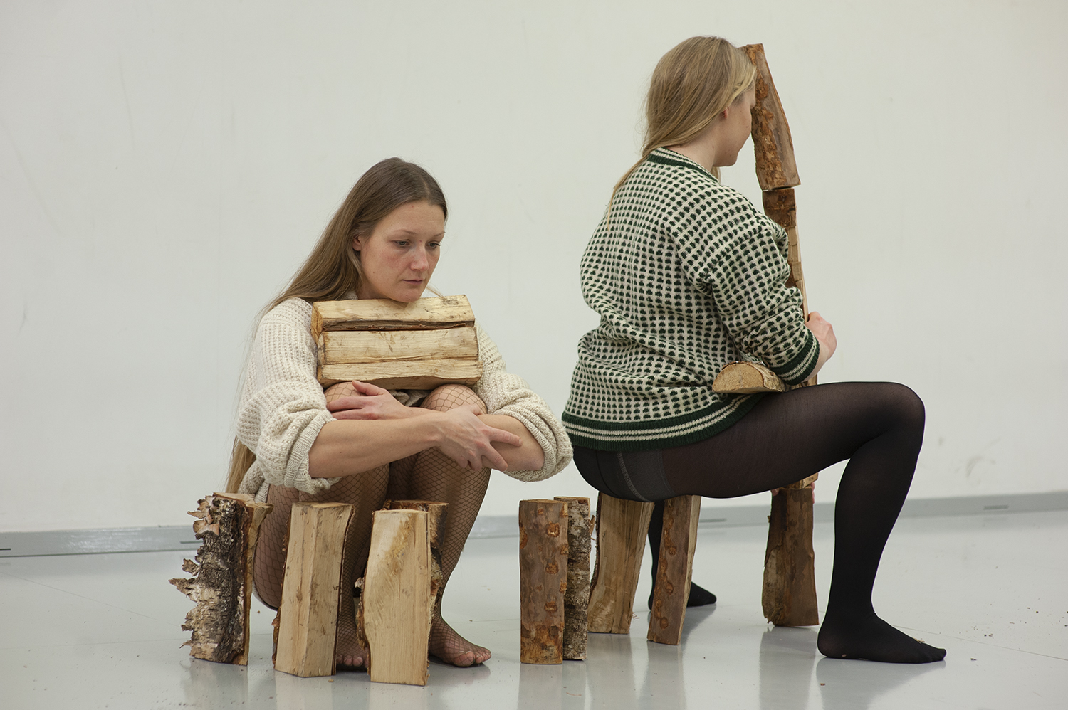 Two assumed women, sitting with blocks of wood in their lap and around them.